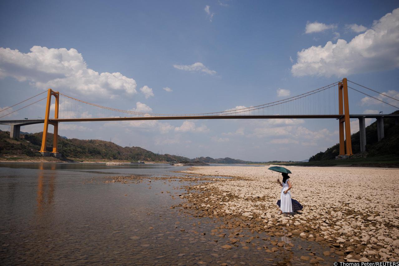 Local resident Zhong watches her husband swim in the river, from the dry riverbed of the Yangtze river that is approaching record-low water levels during a regional drought in Chongqing