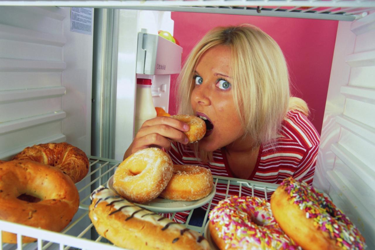 'Portrait of a young woman eating a doughnut in the refrigerator'