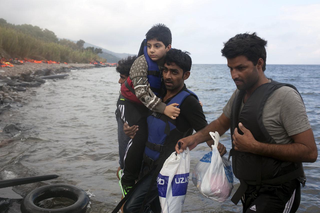 A Pakistani migrant (C) holds a boy after arriving on an overcrowded dinghy under heavy rainfall on the Greek island of Lesbos after crossing a part of the Aegean Sea from the Turkish coast, September 28, 2015. A record number of at least 430,000 refugees
