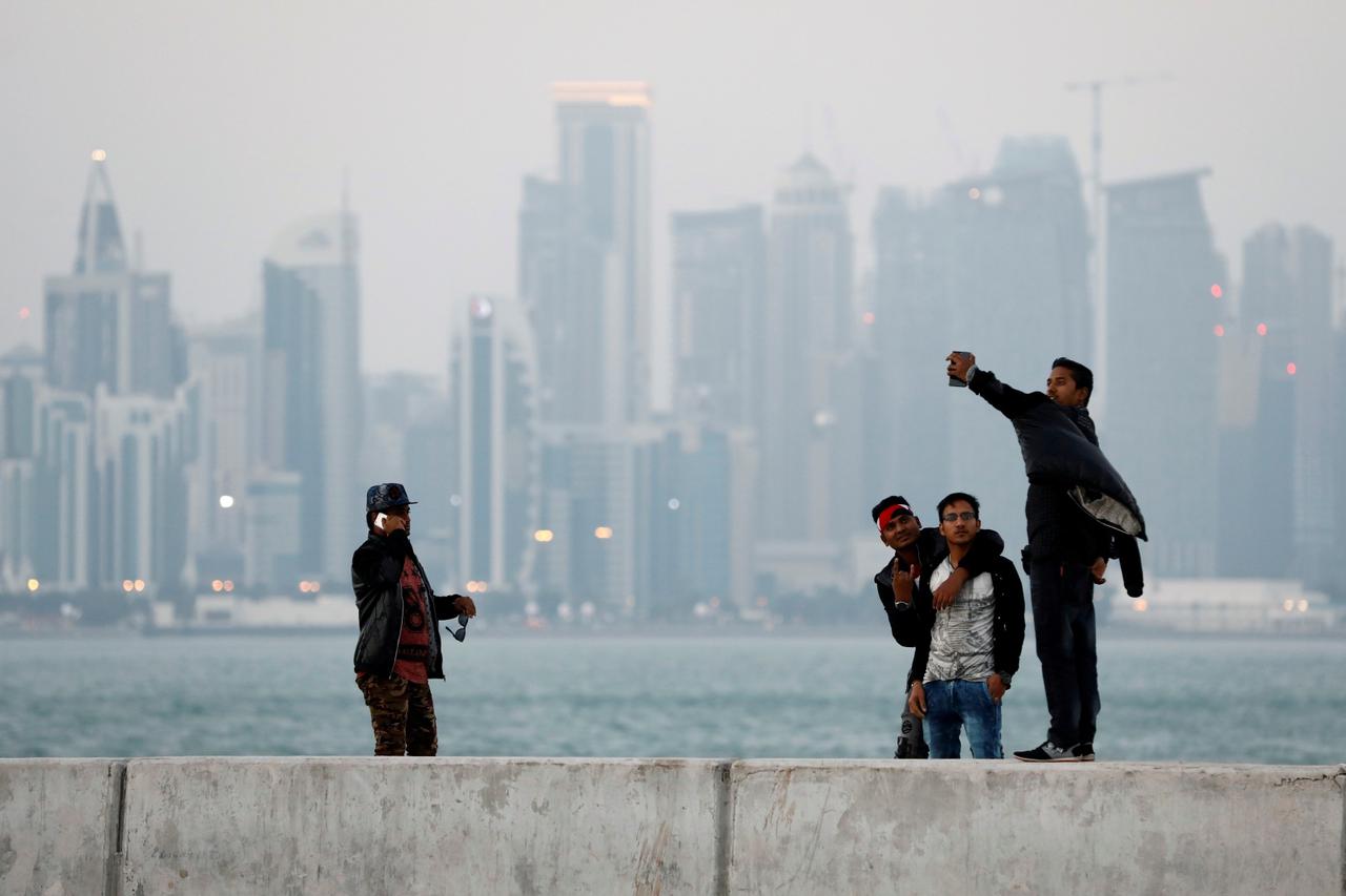 FILE PHOTO: Men take selfies near the sea in front of the skyline of Doha