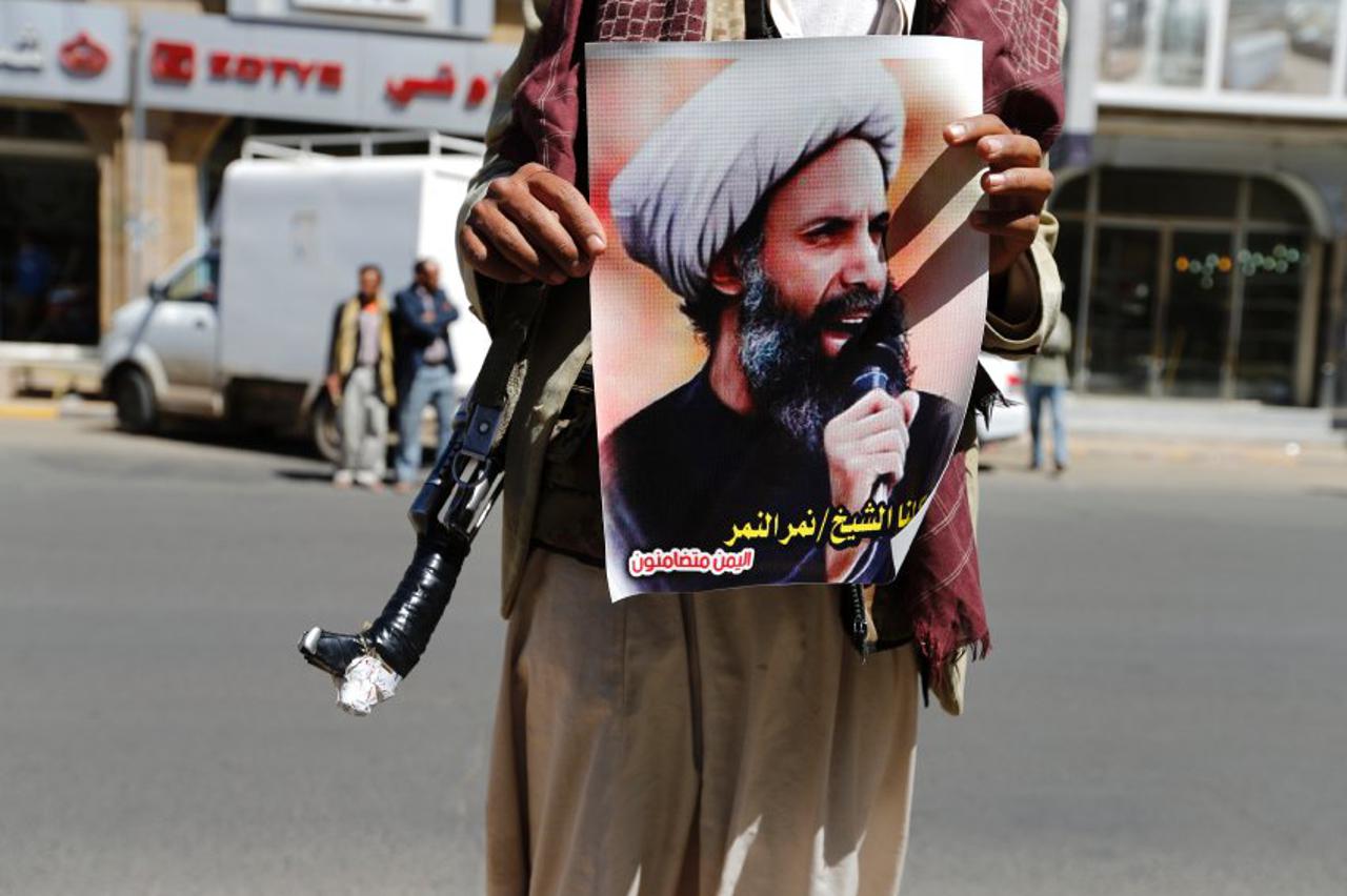 An armed Shi'ite protester holds a poster of Sheikh Nimr al-Nimr during a demonstration outside the Saudi embassy in Sanaa October 18, 2014. Dozens of armed Yemeni Shi'ite Houthi demonstrators protested in front of the Saudi embassy in Sanaa on Saturday c