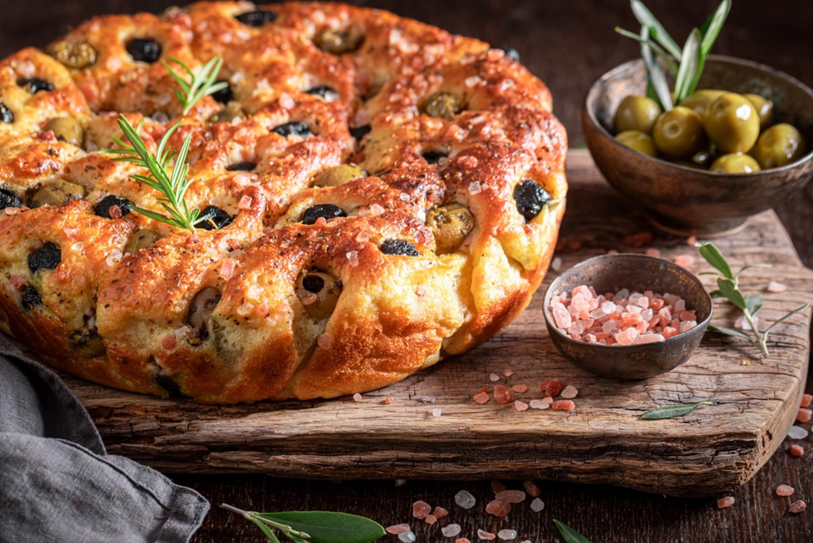 Focaccia s maslinama i krupnom soli: Tijesto za kruh razvucite na limu, prstima napravite udubine i pokapajte maslinovim uljem. Utisnite masline, dodajte ružmarin i pospite krupnom solju. Pecite dok focaccia ne dobije zlatne rubove i dok se miris kruha ne proširi po cijeloj kući. Najbolja je mlaka, ali i sutradan briljira kao odlična podloga za sendviče.
