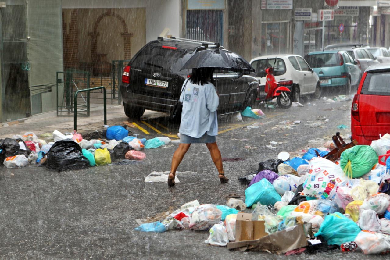 'epa02960799 A pedestrian walks by a pile of garbage under heavy rainfall in Piraeus, Greece on 10 October 2011. Transport came to a standstill on 10 October, and municipal workers said they would ext