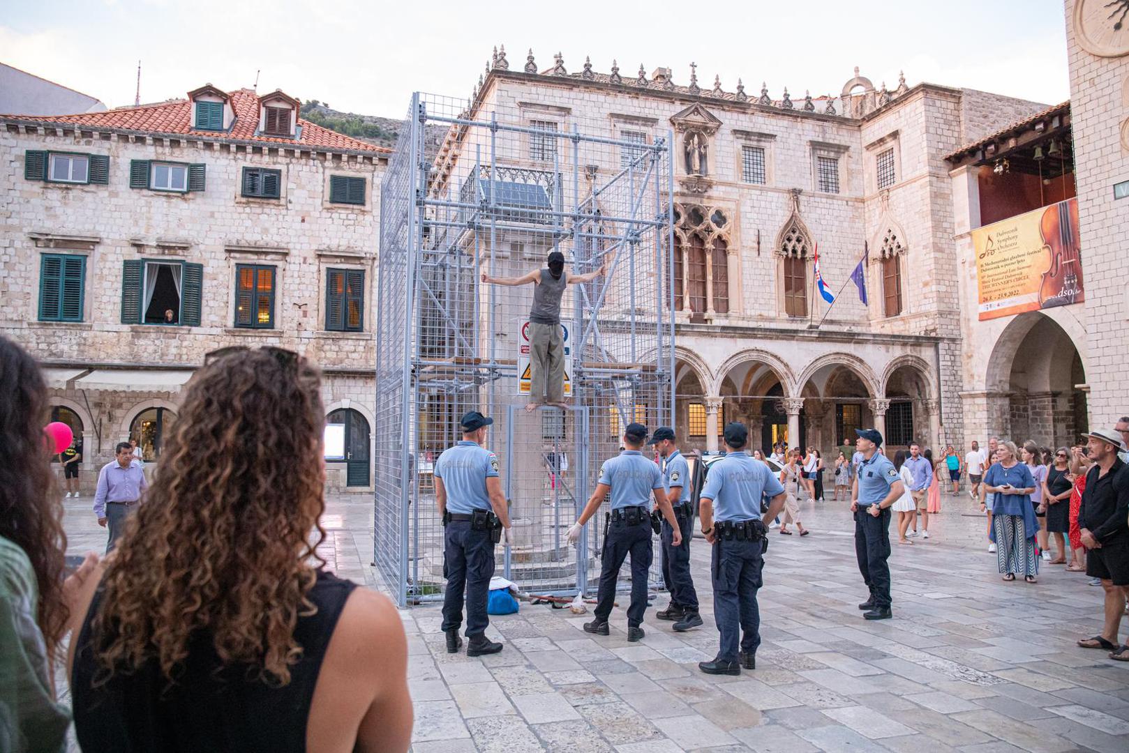 04.09.2022., Orlandov stup, Dubrovnik - Nepoznati ‘performer‘ koji je glavu sakrio popeo se na ogradu kojom je zasticen spomenik Orlando u povijesnoj jezgri Dubrovnika. Muskarac je mirno stajao na ogradi vise od pola sata, nije komunicirao niti je poznato što je svojim postupkom zeli poruciti ili postici. No, na njegov je performas reagirala policija. Dva policajca nisu ga uspjela nagovoriti da se spusti, no uz pojacanje muskarac je spusten s ograde i odvezen u policijskom vozilu.  Photo: Grgo Jelavic/PIXSELL