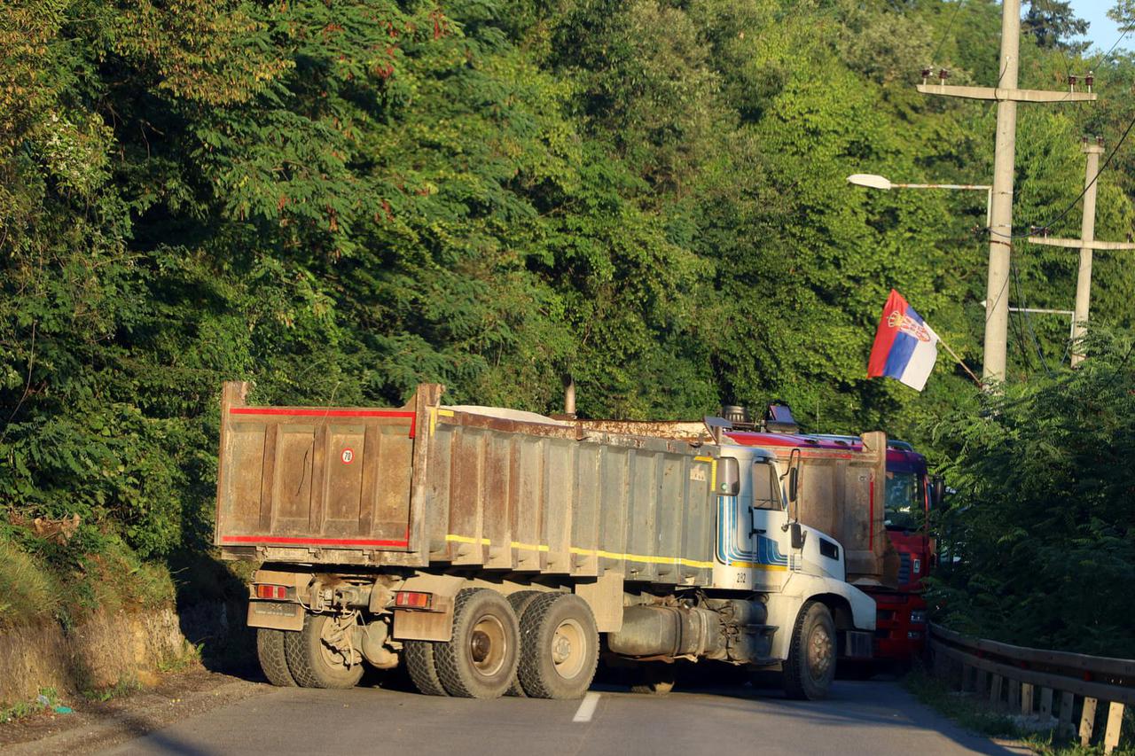 A Serbian flag is seen as trucks block a road in Zupce