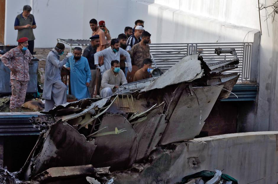 People stand next to the debris of a plane after crashed in a residential area near an airport in Karachi