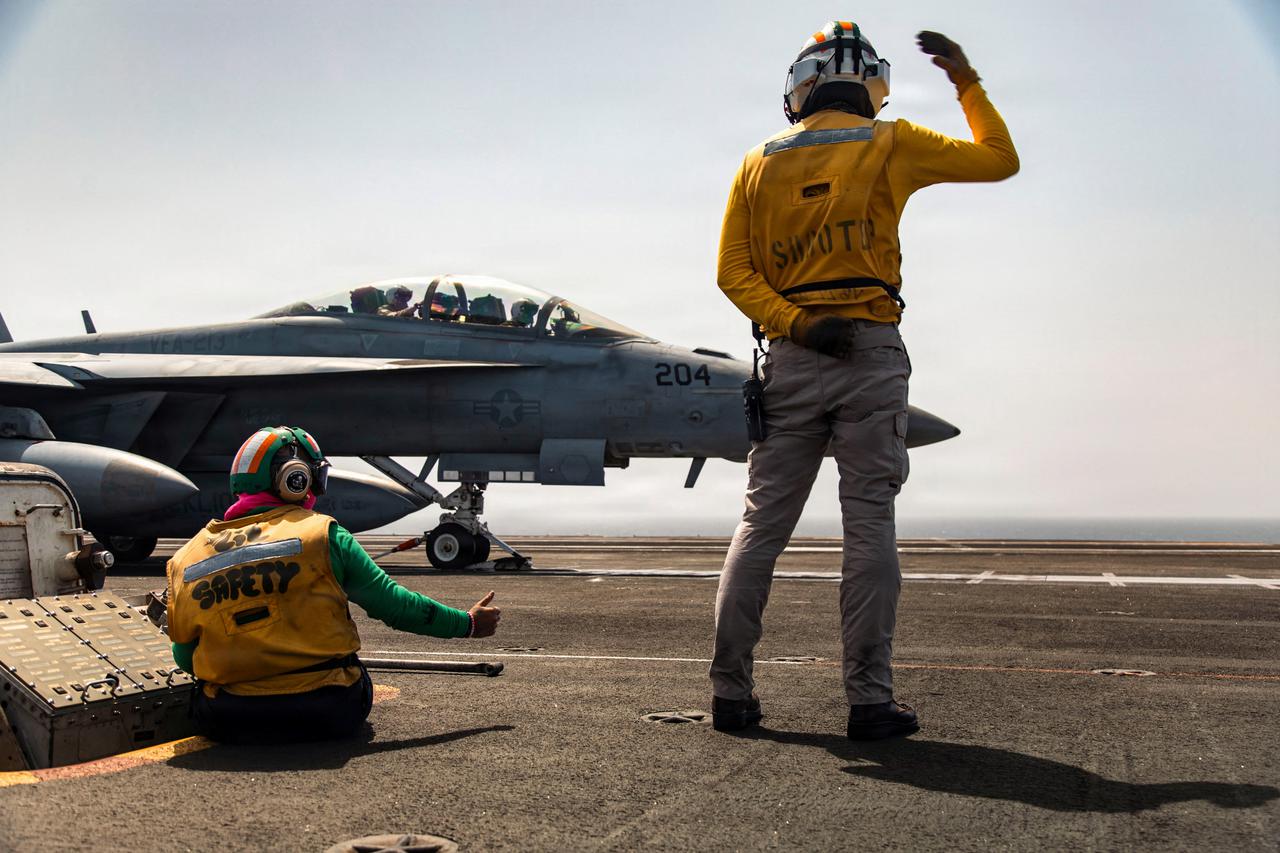 U.S. sailors signal to an F/A-18F Super Hornet aircraft