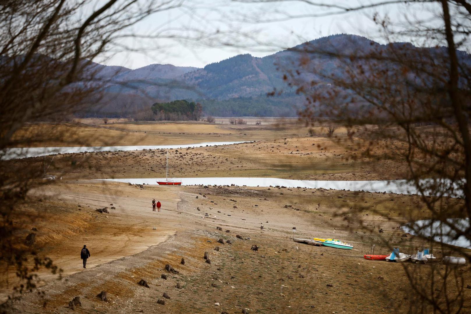 People walk on the banks of the partially dry Lake Montbel at the foot of the Pyrenees Mountains as France faces records winter dry spell raising fears of another summer of droughts and water restrictions, March 13, 2023. REUTERS/Sarah Meyssonnier Photo: Sarah Meyssonnier/REUTERS