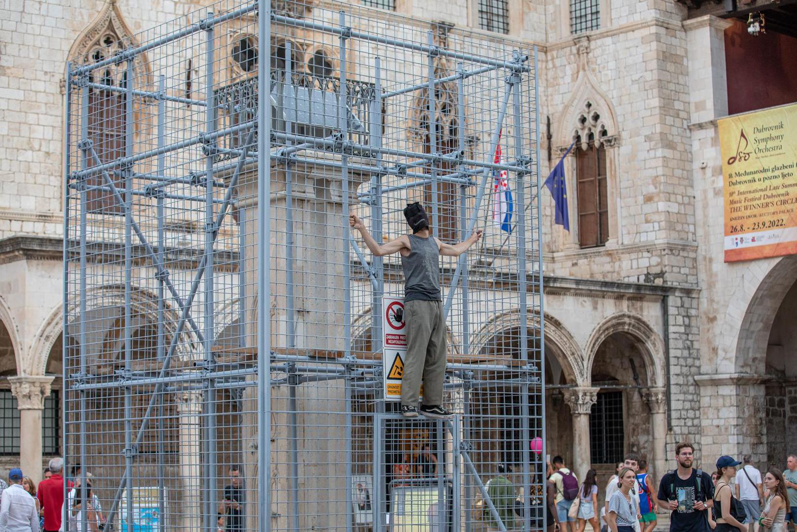 04.09.2022., Orlandov stup, Dubrovnik - Nepoznati ‘performer‘ koji je glavu sakrio popeo se na ogradu kojom je zasticen spomenik Orlando u povijesnoj jezgri Dubrovnika. Muskarac je mirno stajao na ogradi vise od pola sata, nije komunicirao niti je poznato što je svojim postupkom zeli poruciti ili postici. No, na njegov je performas reagirala policija. Dva policajca nisu ga uspjela nagovoriti da se spusti, no uz pojacanje muskarac je spusten s ograde i odvezen u policijskom vozilu.  Photo: Grgo Jelavic/PIXSELL