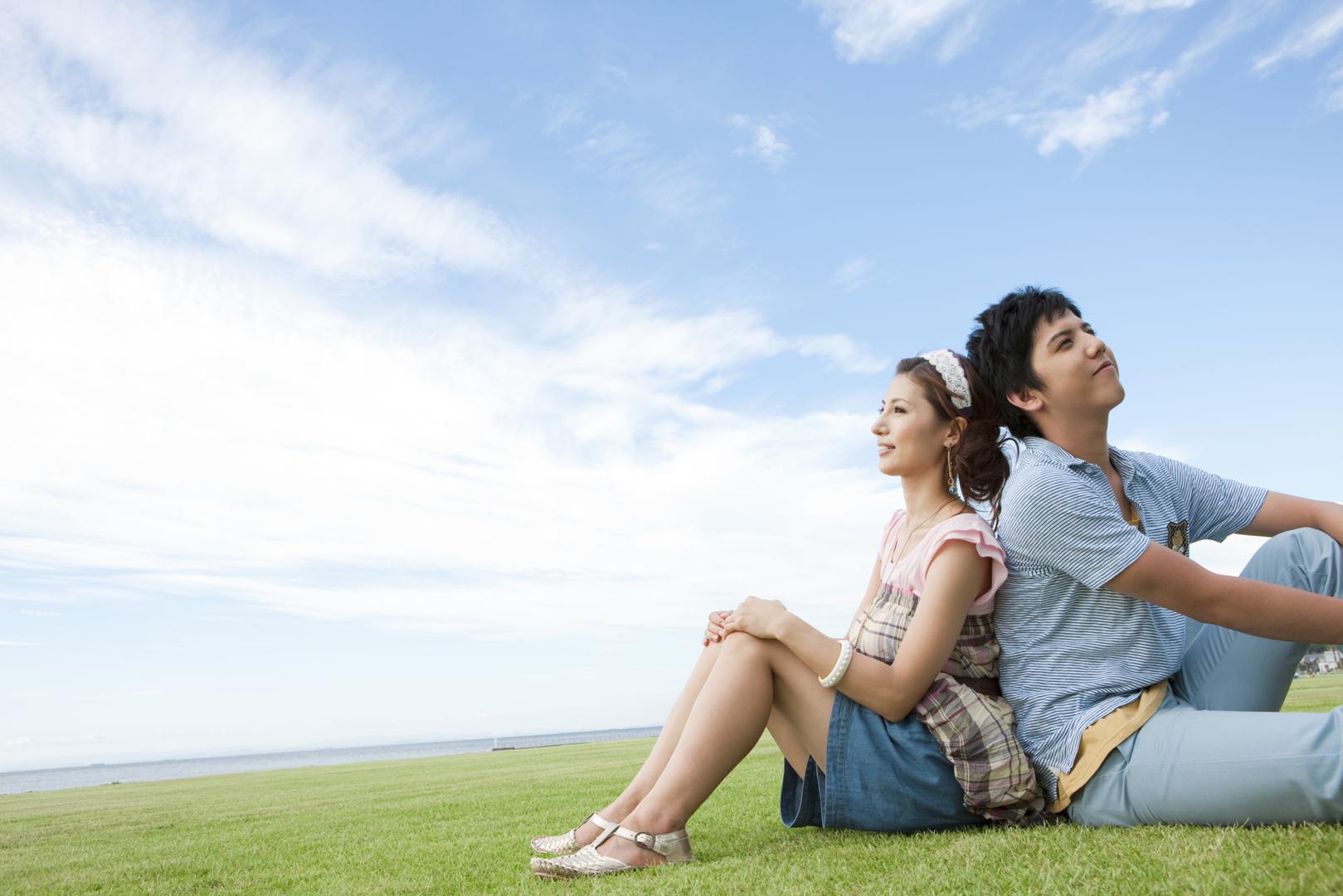 Back coupling. Sitting on the grass. People sitting on the grass. Young man sitting on the ground. Young girl sitting on the ground.