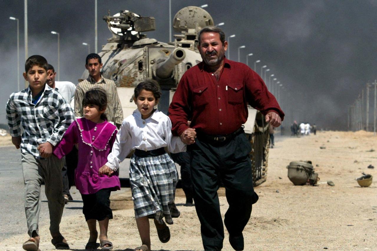 A family flees past a destroyed Iraqi T-55 tank after a mortar attack on British Army positions in the southern city of Basra, Iraq