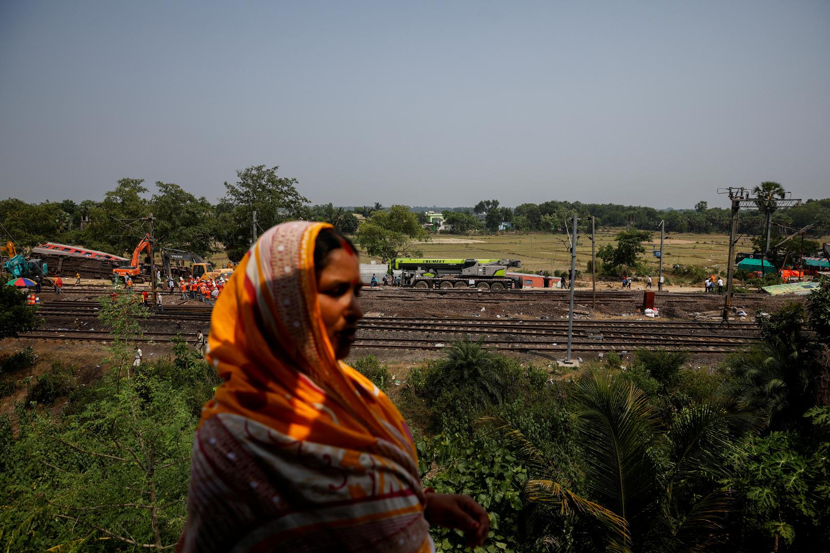 A woman stands on the roof of a house as heavy machinery removes damaged coaches from the railway tracks at the site of a train collision following the accident in Balasore district in the eastern state of Odisha, India, June 4, 2023. REUTERS/Adnan Abidi Photo: ADNAN ABIDI/REUTERS