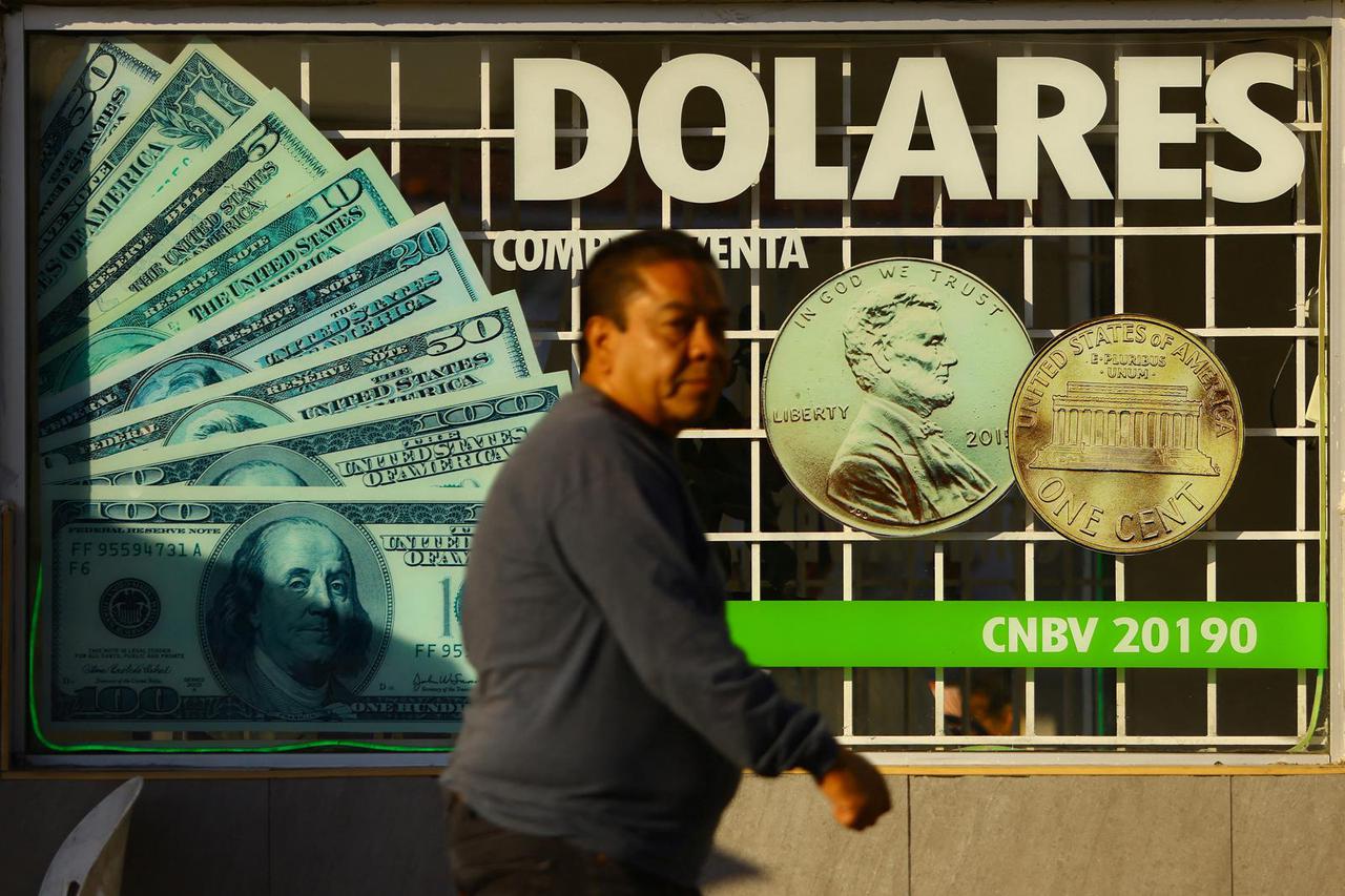 A man walks past drawings of dollars outside a foreign exchange house in Ciudad Juarez