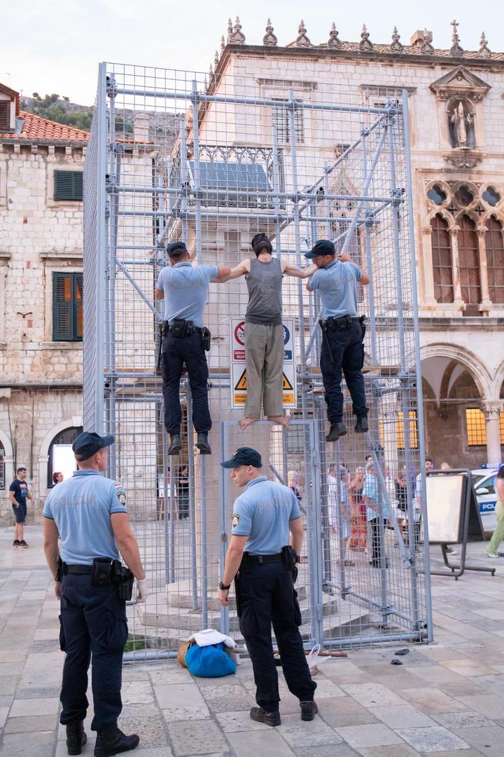 04.09.2022., Orlandov stup, Dubrovnik - Nepoznati ‘performer‘ koji je glavu sakrio popeo se na ogradu kojom je zasticen spomenik Orlando u povijesnoj jezgri Dubrovnika. Muskarac je mirno stajao na ogradi vise od pola sata, nije komunicirao niti je poznato što je svojim postupkom zeli poruciti ili postici. No, na njegov je performas reagirala policija. Dva policajca nisu ga uspjela nagovoriti da se spusti, no uz pojacanje muskarac je spusten s ograde i odvezen u policijskom vozilu.  Photo: Grgo Jelavic/PIXSELL
