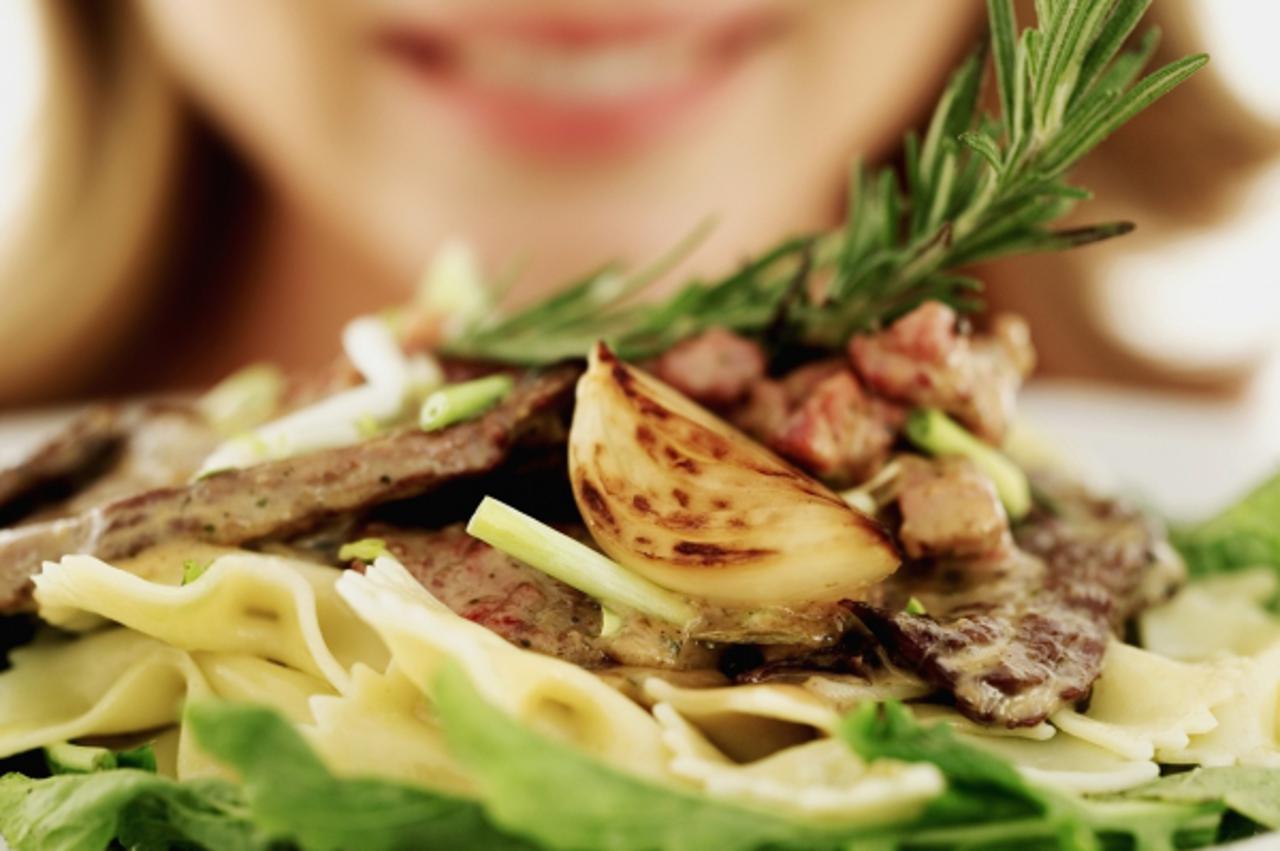 'close-up of a young woman holding a plate of steak with pasta and vegetables'