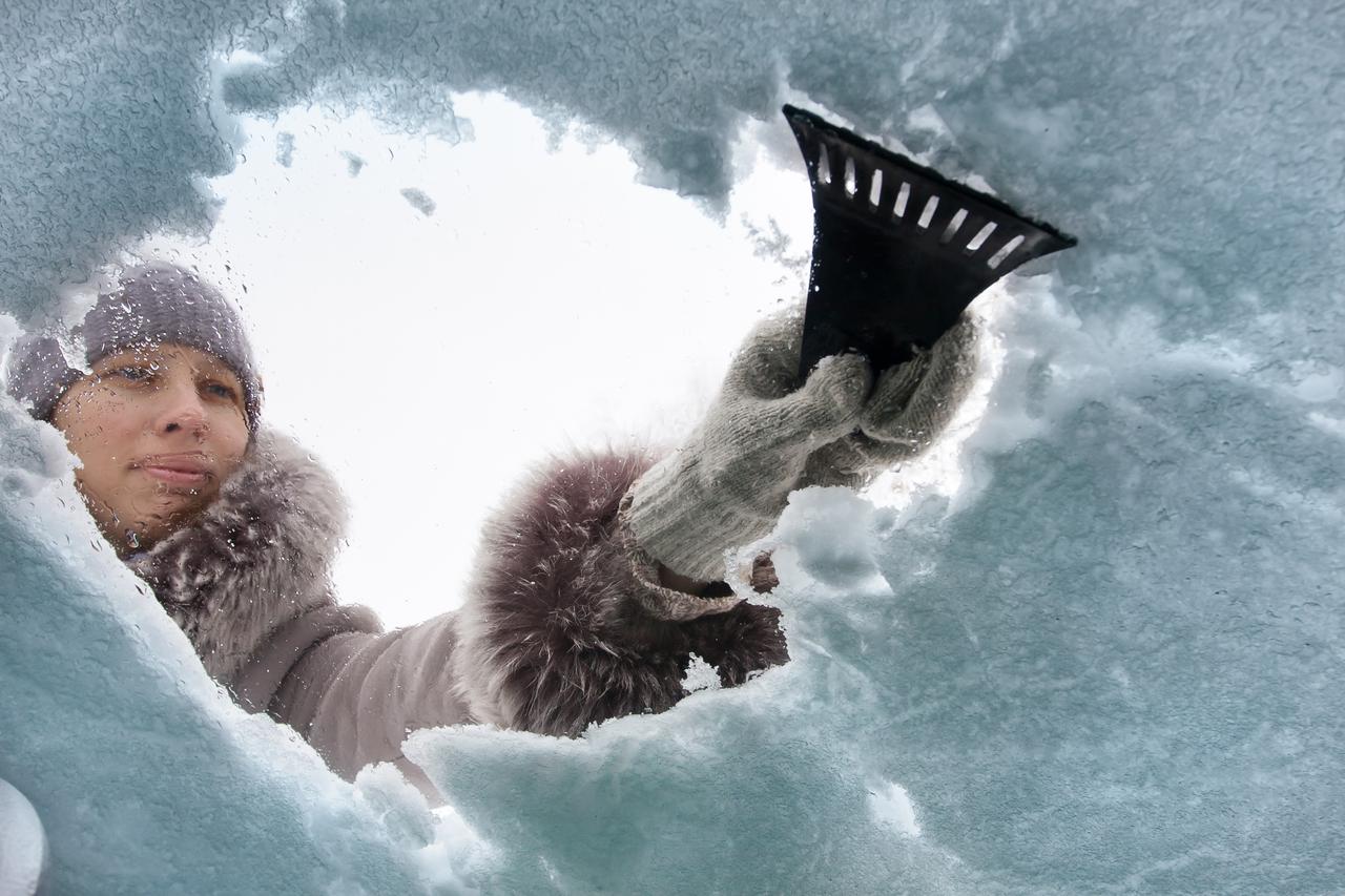 woman cleaning window of car from the snow with scraper