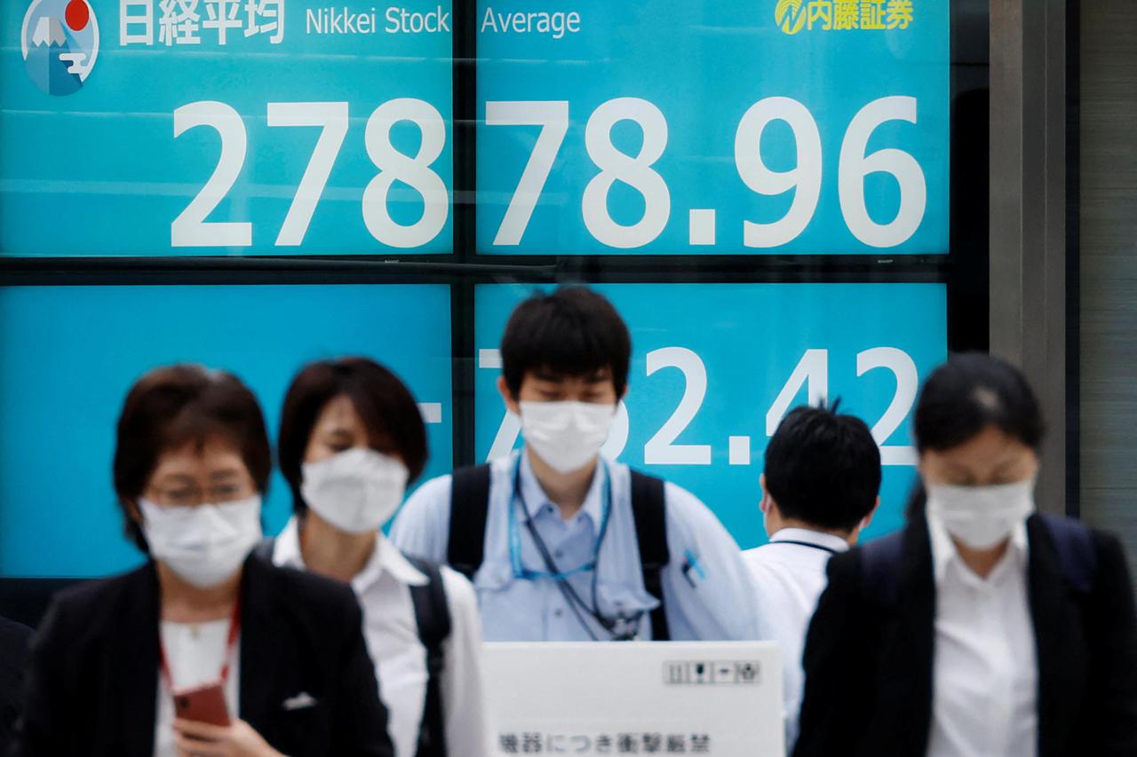 Pedestrians wearing protective masks amid the coronavirus disease (COVID-19) outbreak, walk past an electronic board displaying Japan's Nikkei index outside a brokerage in Tokyo