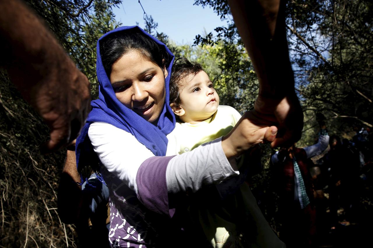 A Syrian refugee holding a baby is helped to climb a slope, moments after arriving on a dinghy on the Greek island of Lesbos, September 16, 2015. Two decades of frontier-free travel across Europe unraveled on Monday as countries re-established border cont