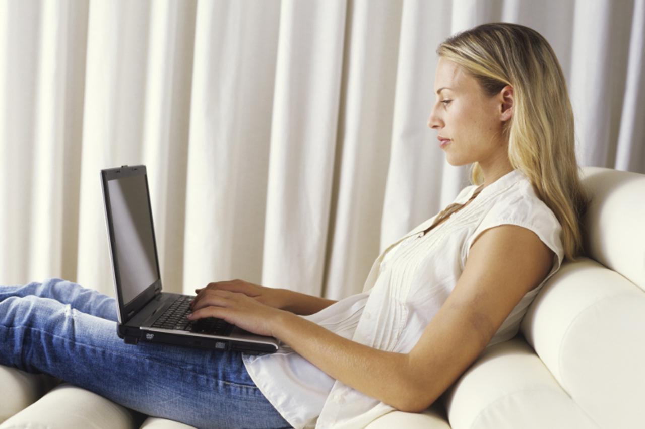 'Young woman sitting on reclining chair using laptop, side view'