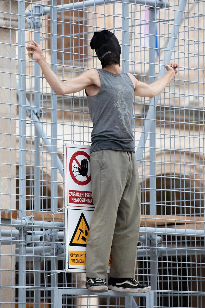 04.09.2022., Orlandov stup, Dubrovnik - Nepoznati ‘performer‘ koji je glavu sakrio popeo se na ogradu kojom je zasticen spomenik Orlando u povijesnoj jezgri Dubrovnika. Muskarac je mirno stajao na ogradi vise od pola sata, nije komunicirao niti je poznato što je svojim postupkom zeli poruciti ili postici. No, na njegov je performas reagirala policija. Dva policajca nisu ga uspjela nagovoriti da se spusti, no uz pojacanje muskarac je spusten s ograde i odvezen u policijskom vozilu.  Photo: Grgo Jelavic/PIXSELL