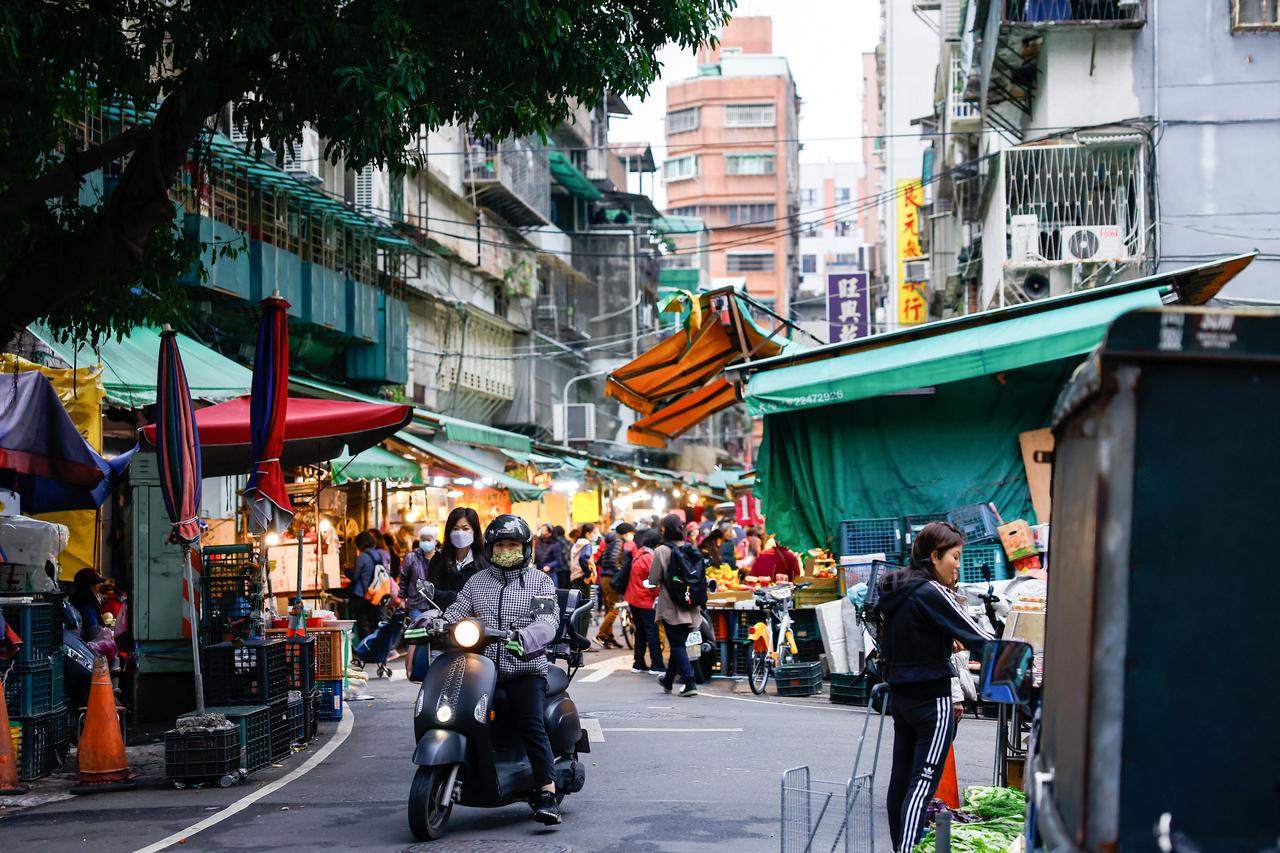 A woman on a motorbike rides at a morning market in Taipei