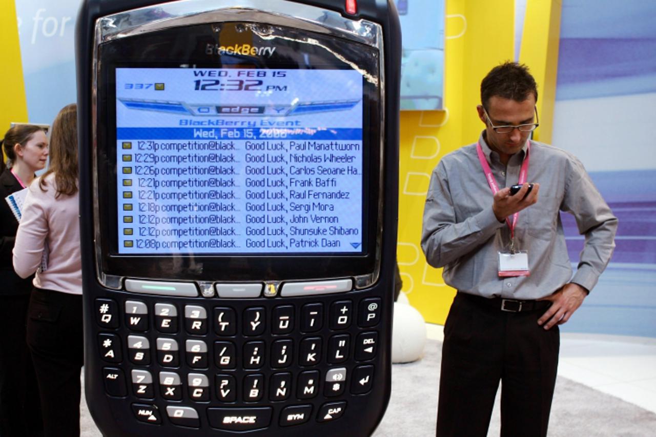 \'A visitor looks at a phone as he stands next to a display of the new BlackBerry 8700 at 3GSM World Congress in Barcelona, Spain February 15, 2006. The 3GSM World Congress, which is attended by every