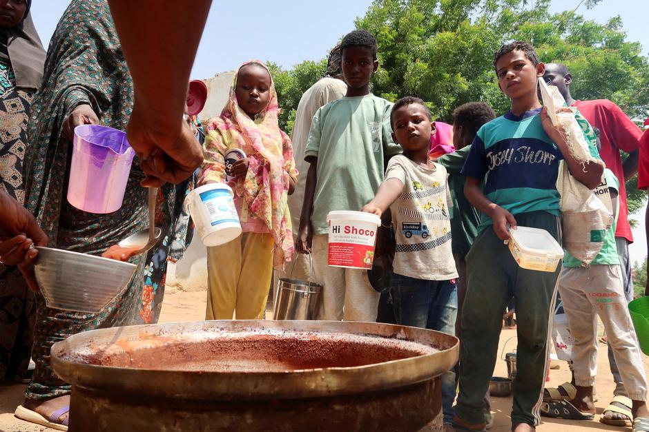 FILE PHOTO: People hold pots as volunteers distribute food in Omdurman