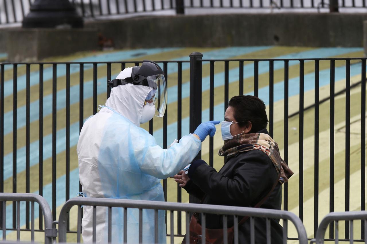 A Hospital worker distributes PPE to people waiting in line to be tested for coronavirus (COVID-19) outside Elmhurst Hospital Center in New York