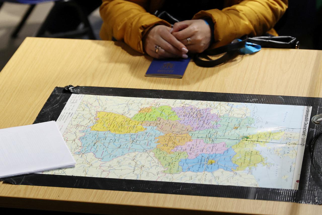 A woman sits with her passport in front of a map of Germany at the arrival and temporary accommodation centre for Ukrainian refugees at the former Tegel airport in Berlin