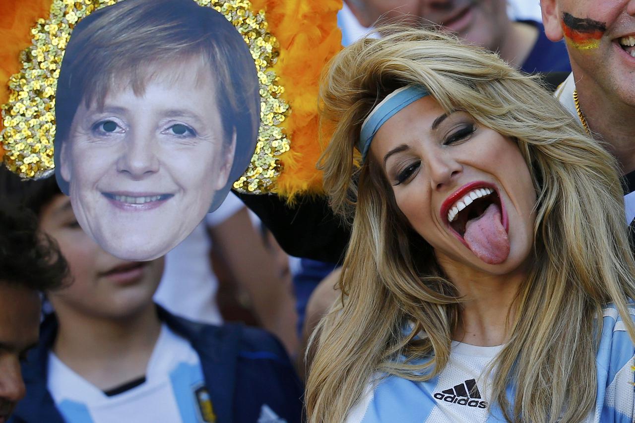 An Argentina fan reacts near a mask of German Chancellor Angela Merkel before the team's 2014 World Cup final against Germany at the Maracana stadium in Rio de Janeiro July 13, 2014. REUTERS/Kai Pfaffenbach (BRAZIL  - Tags: SOCCER SPORT WORLD CUP)