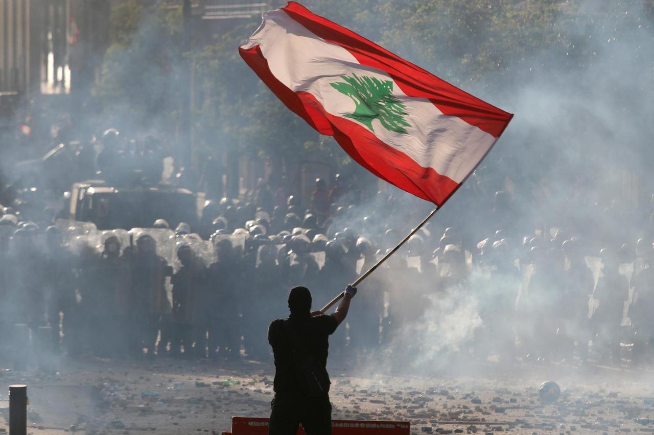 A demonstrator waves the Lebanese flag in front of riot police during a protest in Beirut