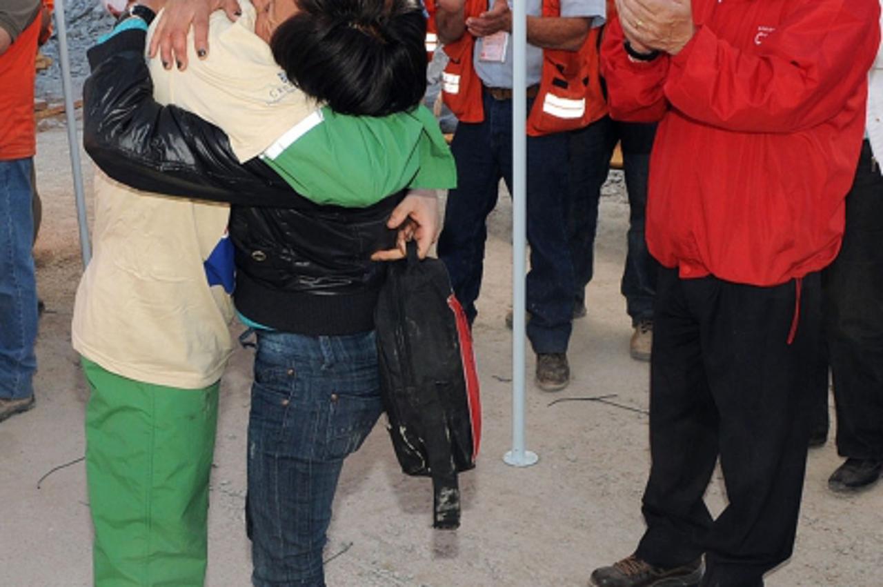 'Handout picture released by Chile\'s presidential press office of Chilean President Sebastian Pinera (R) smiling as Chilean miner Carlos Bugueno (L) is hugged by his mother after being brought to the