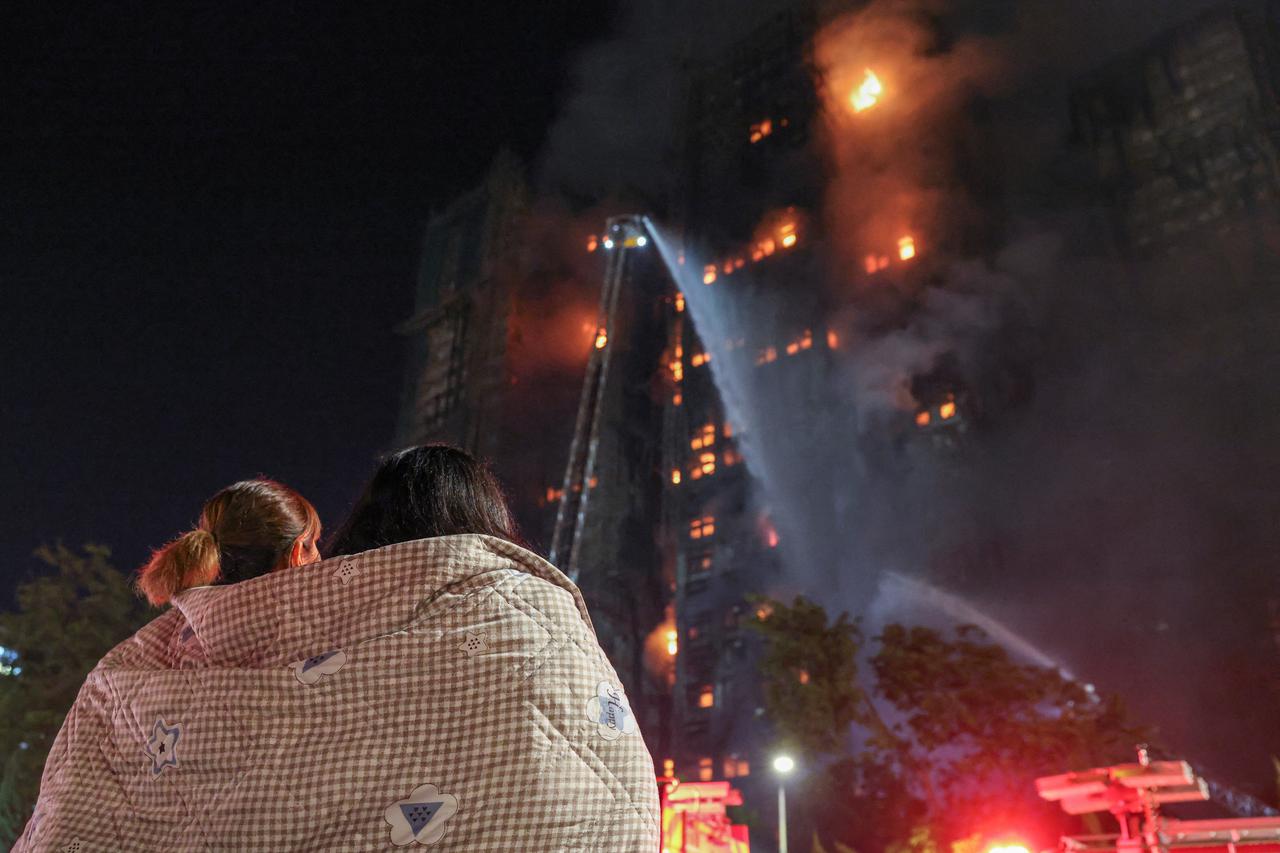 Residents wrapped in blankets watch flames engulf bamboo scaffolding at Wang Fuk Court housing estate after a major fire broke out, in Tai Po, Hong Kong