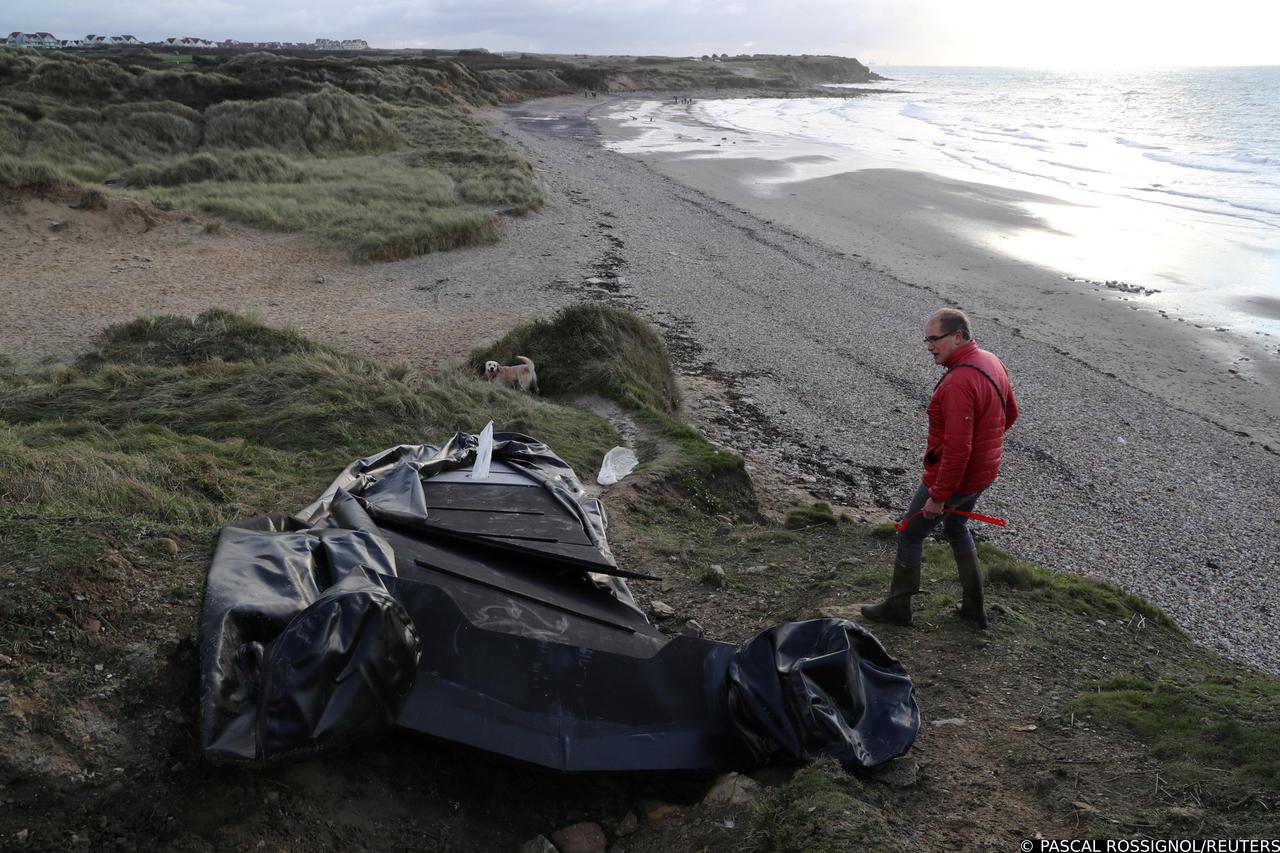 A man walks past a damaged inflatable dinghy in the Slack dunes in Wimereux